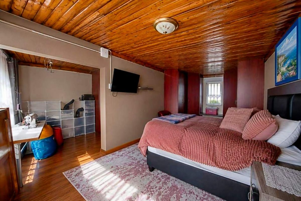 A bedroom featuring a distinctive timber-clad ceiling, built-in storage cupboards, and laminate flooring, with an adjoining alcove area.