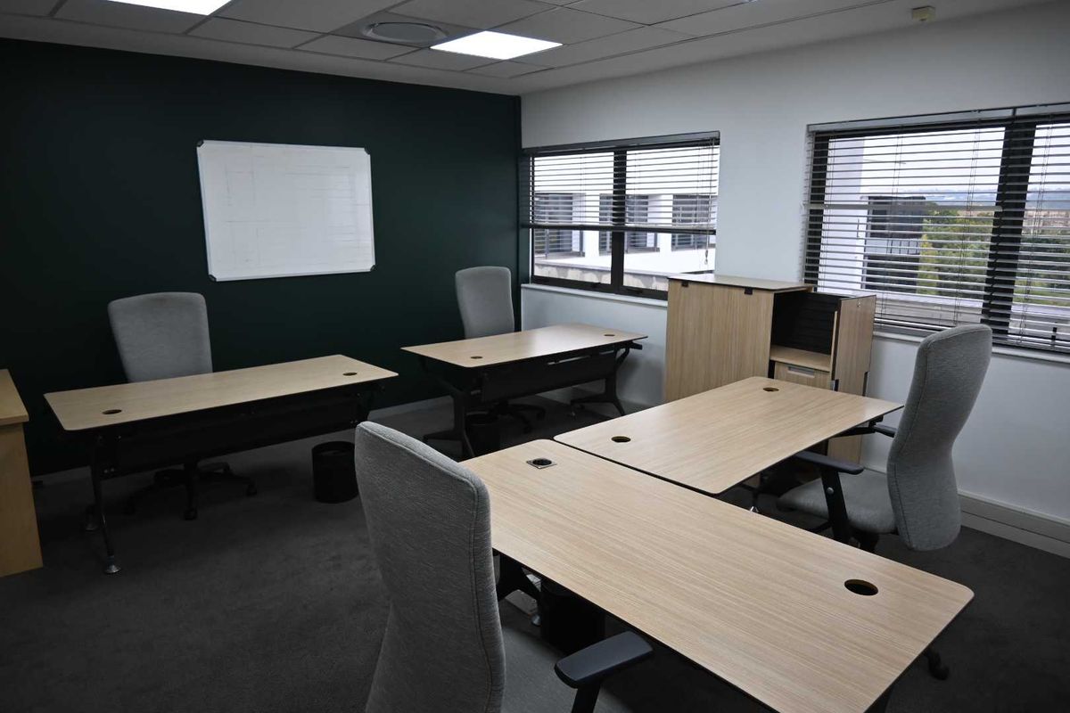 A professional office space featuring recessed ceiling lighting, dark accent wall, carpeted flooring, and large windows with venetian blinds.