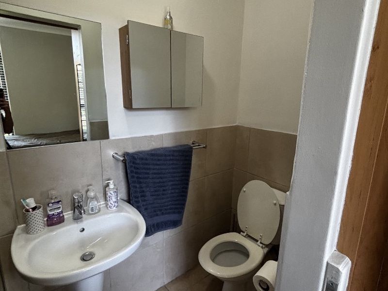 A functional bathroom featuring a pedestal washbasin, toilet, and wall-mounted medicine cabinet with neutral wall and floor tiling.