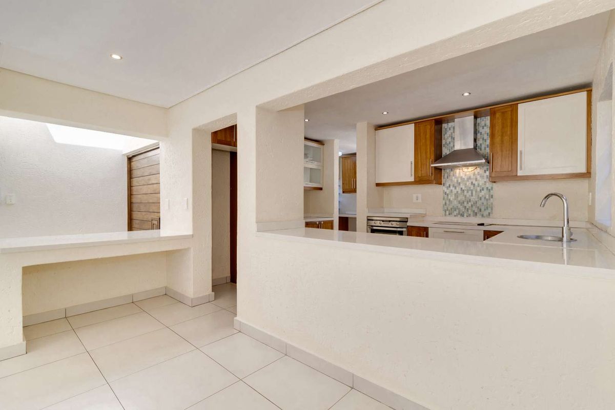 A clean, functional kitchen featuring built-in cabinetry, stone countertops, a mosaic tile splashback, and integrated stainless steel appliances with a breakfast bar opening.