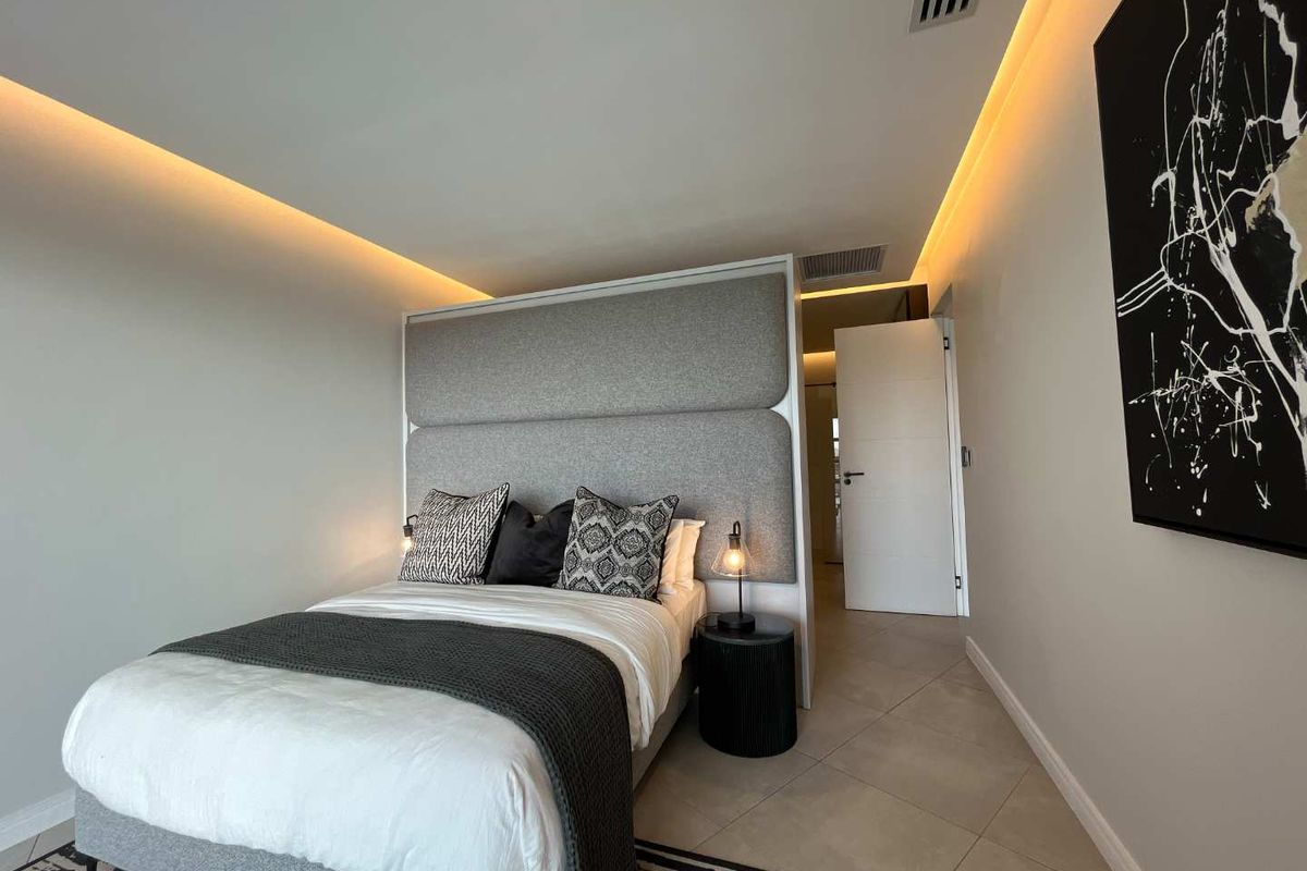 Modern bedroom featuring a large upholstered headboard, recessed ambient ceiling lighting, ducted air conditioning, and neutral tiled flooring.