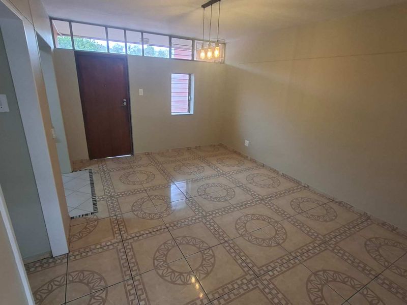 An empty, well-lit living area featuring patterned ceramic floor tiles, a solid entrance door, and high-level transom windows providing natural light.