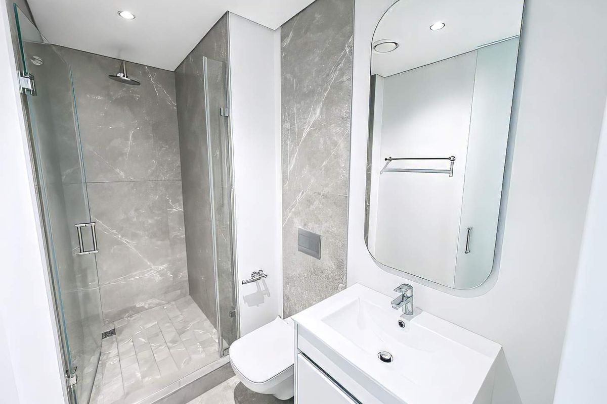 Modern bathroom featuring a glass-enclosed walk-in shower, wall-mounted toilet, and a sleek vanity with a large mirror and contemporary grey marble-look tiling.