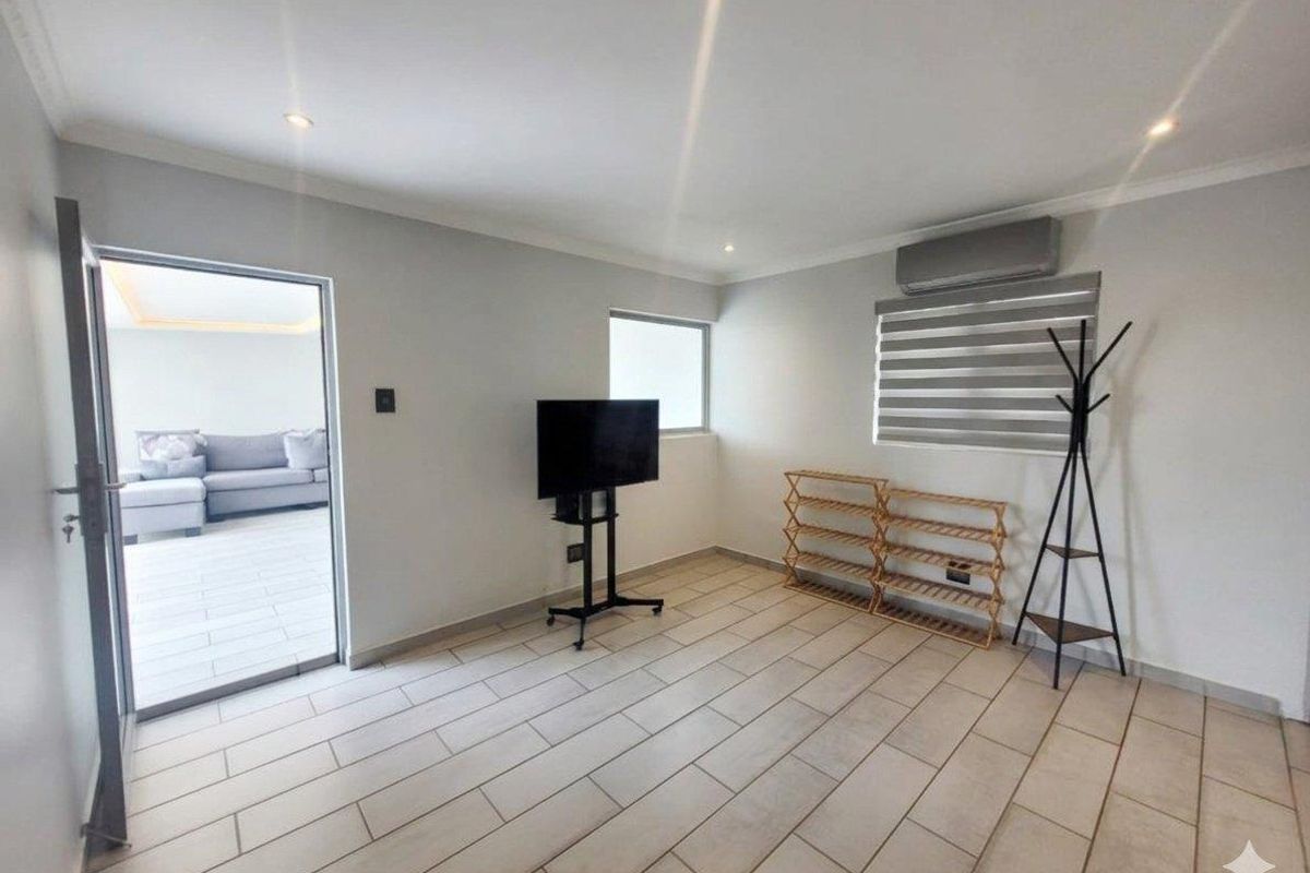 A bright, neutral living area featuring tiled flooring, recessed lighting, and a wall-mounted air conditioning unit, with direct access to an outdoor patio space.