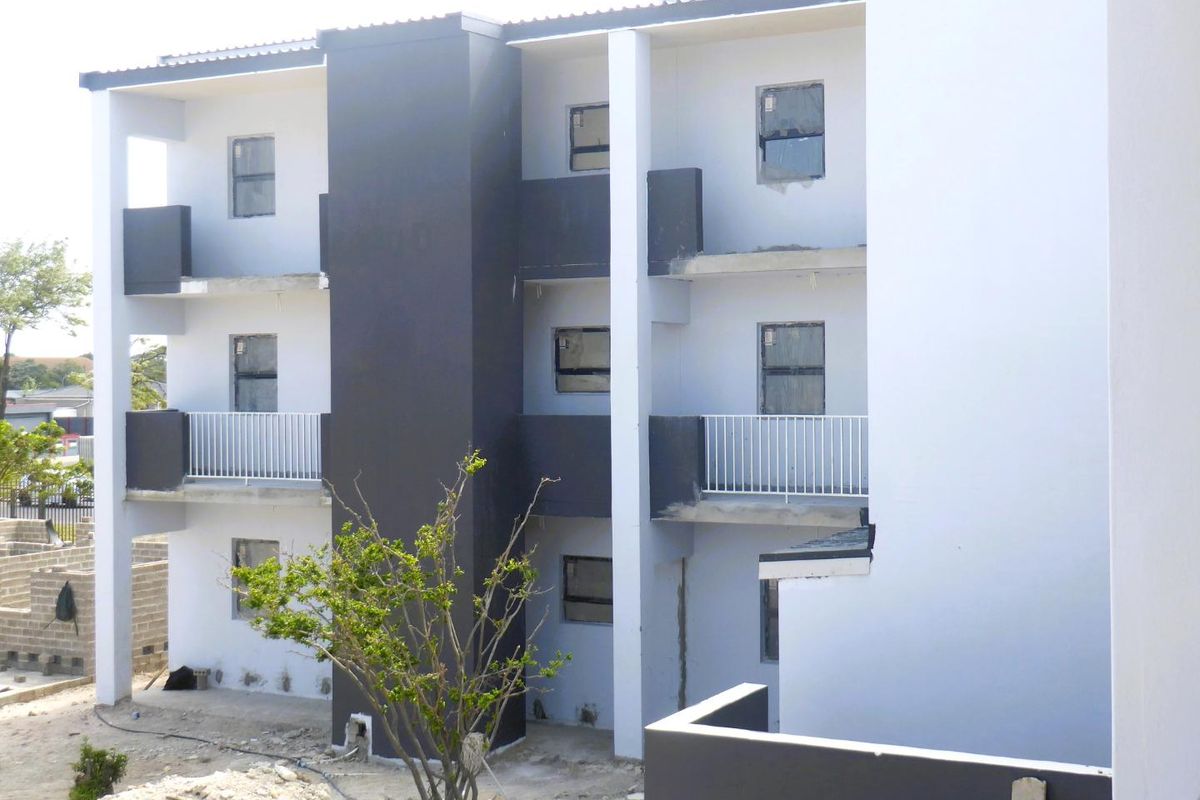 Rear elevation of a multi-story apartment building featuring private balconies with metal railings and modern dark and light exterior paint finishes.