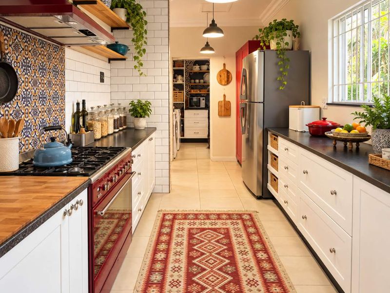 A well-appointed kitchen featuring a red range stove, patterned tile backsplash, white cabinetry, dark countertops, and a scullery area visible in the background.