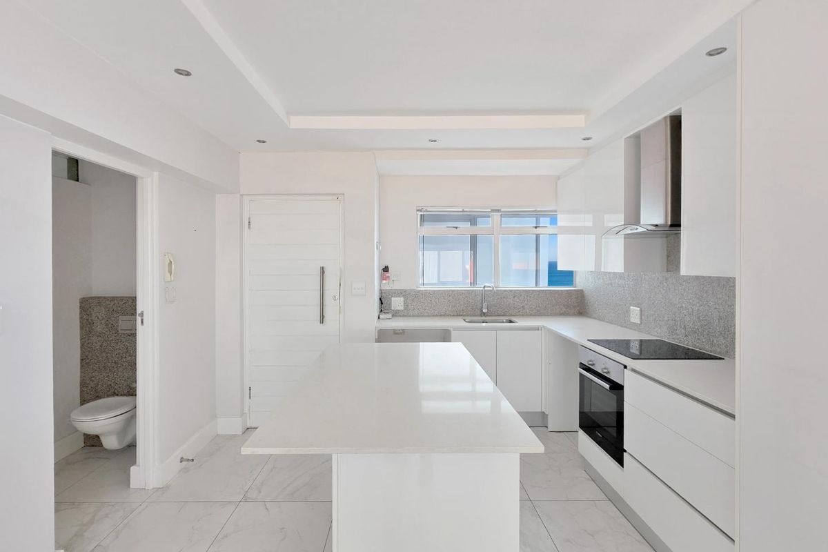 Modern, minimalist kitchen featuring a central island, sleek white cabinetry, stone countertops, integrated appliances, and high-quality tiled flooring.
