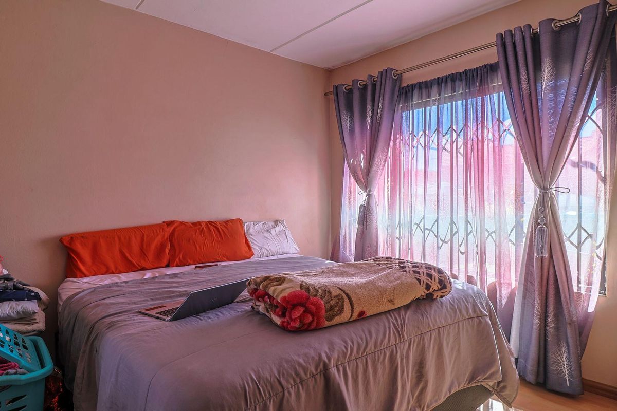 A bedroom featuring a large window with security gate and curtain fixtures, providing natural light and access to the exterior.