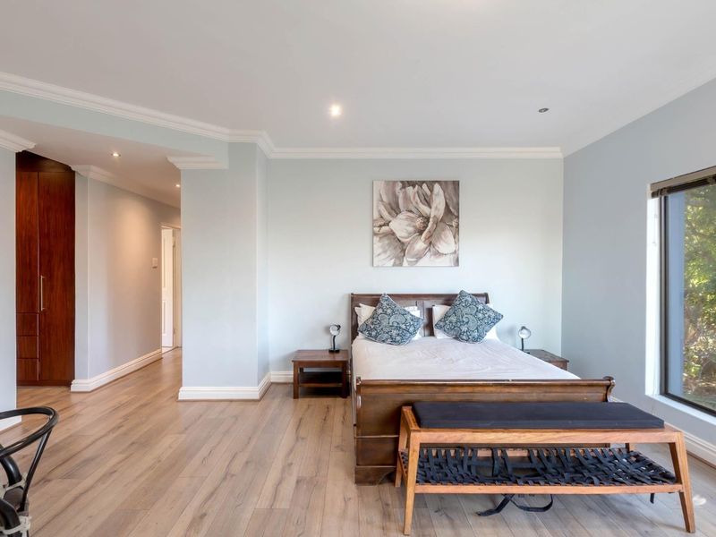 Spacious bedroom featuring light-toned laminate flooring, crown molding, recessed lighting, and a large built-in wardrobe with dark wood finish.