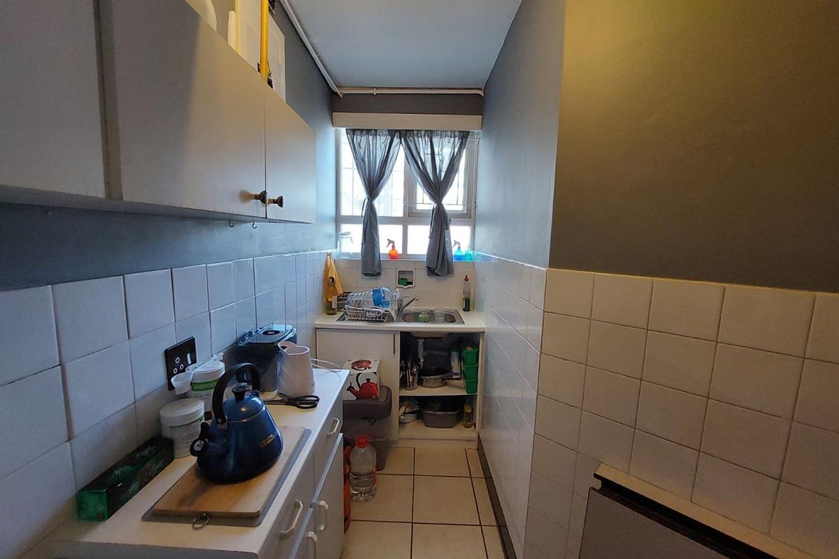 A compact galley-style kitchen featuring tiled splashbacks, built-in cabinetry, and a single basin sink under a window.