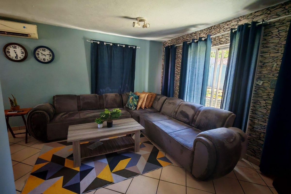 A comfortable living room featuring tiled flooring, a wall-mounted air conditioning unit, and a decorative stone-effect feature wall with large windows.