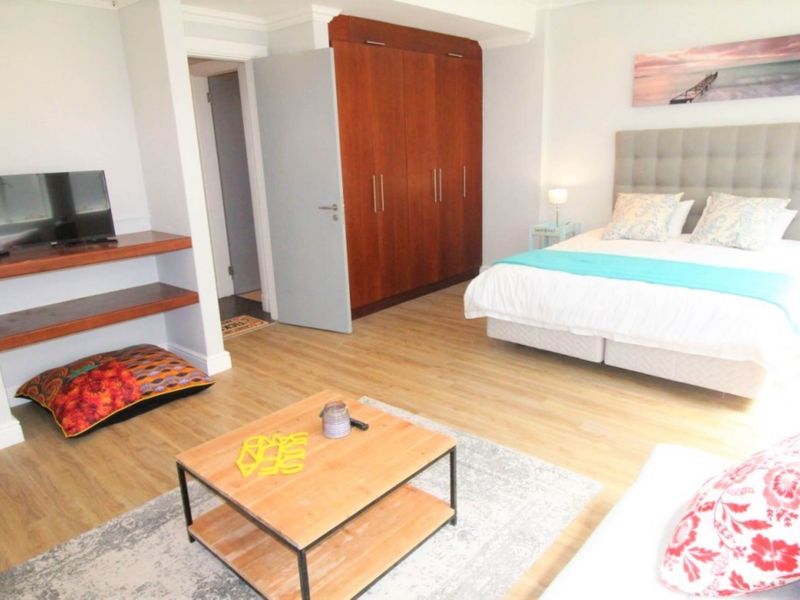 A well-maintained bedroom featuring light laminate flooring, neutral walls, and a large built-in wooden wardrobe providing ample storage space.