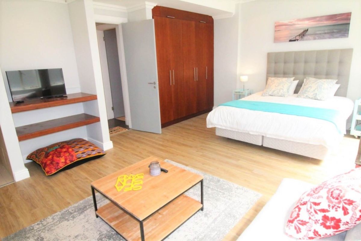 A well-maintained bedroom featuring light laminate flooring, neutral walls, and a large built-in wooden wardrobe providing ample storage space.