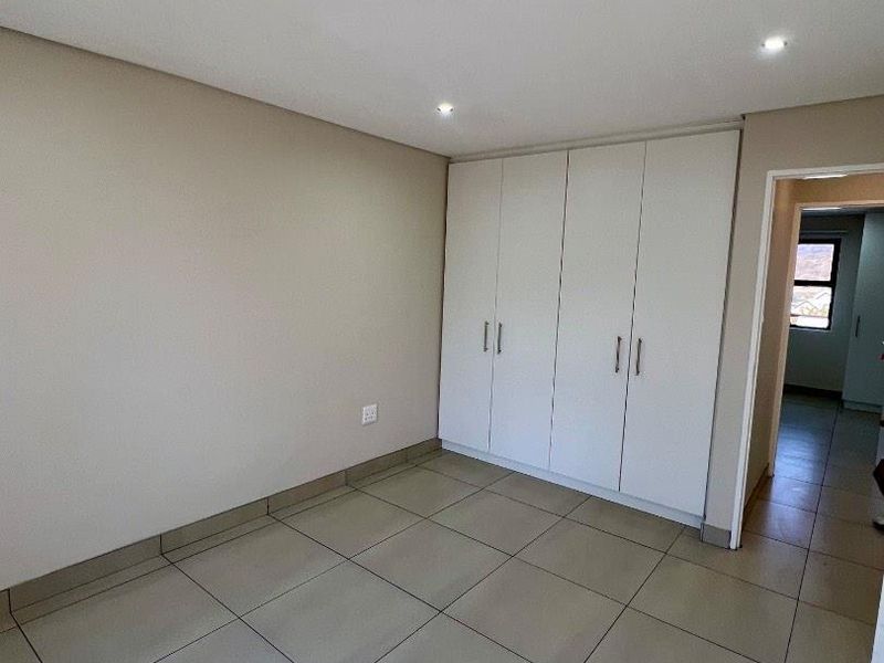 A clean, empty bedroom featuring neutral tiled flooring, built-in cupboards, and modern recessed downlighting.