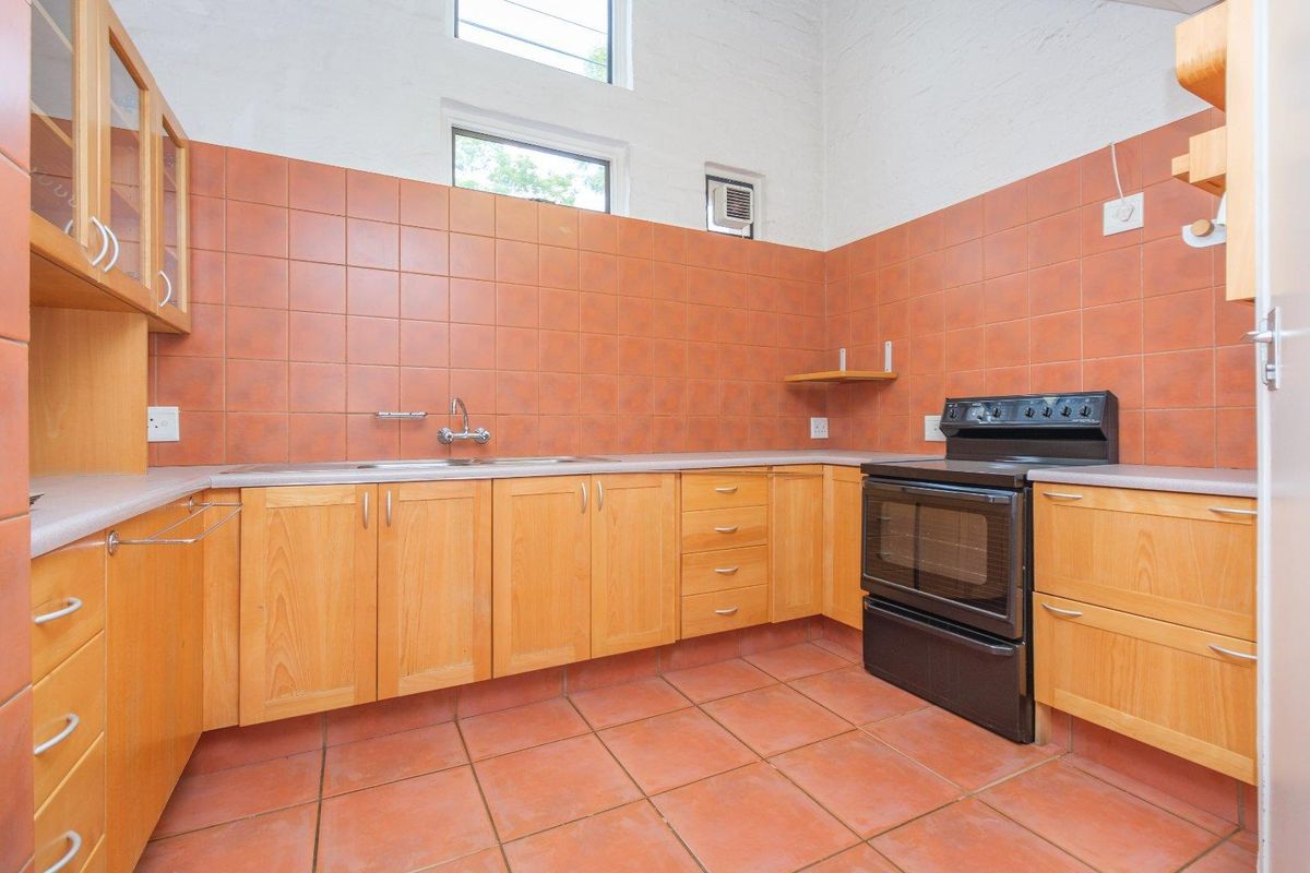 A functional kitchen featuring wooden cabinetry, terracotta-style floor and wall tiling, a built-in sink, and a freestanding oven.