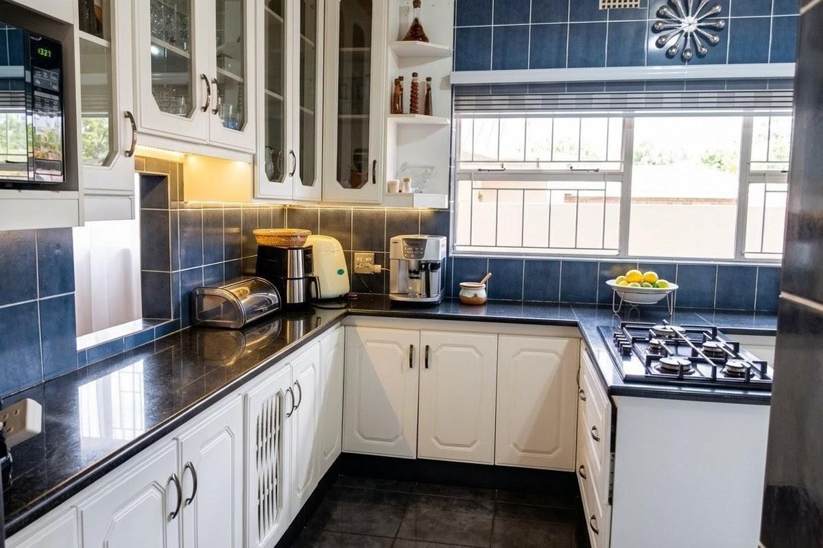 A functional kitchen featuring white cabinetry, dark countertops, blue tiled splashbacks, and a built-in gas hob with an integrated oven.