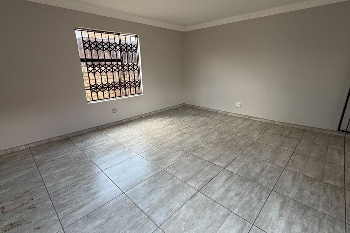 A bright, empty living area featuring neutral wall paint, modern ceramic floor tiles, and secure window and door fittings.
