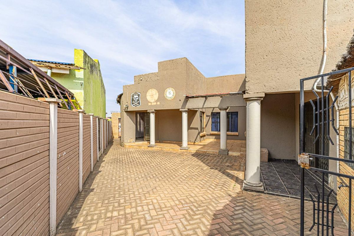 Rear exterior view of the property featuring a paved courtyard, covered patio area with concrete columns, and perimeter boundary walling.