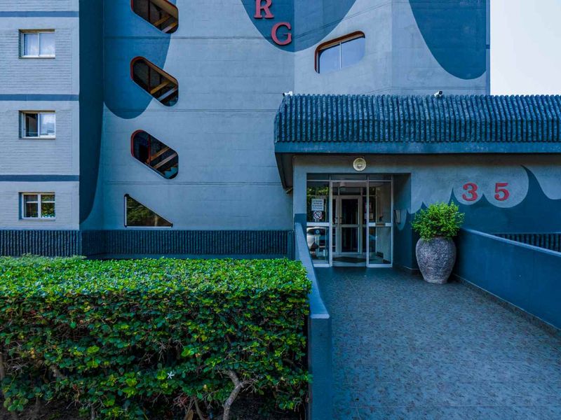 The front entrance of the apartment building features a tiled ramp leading to a glass door, set against a painted exterior facade.
