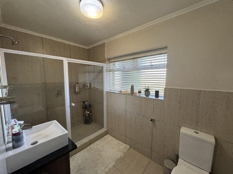 A well-maintained bathroom featuring a glass shower enclosure, modern vessel sink on a vanity, and neutral wall tiling with natural light.