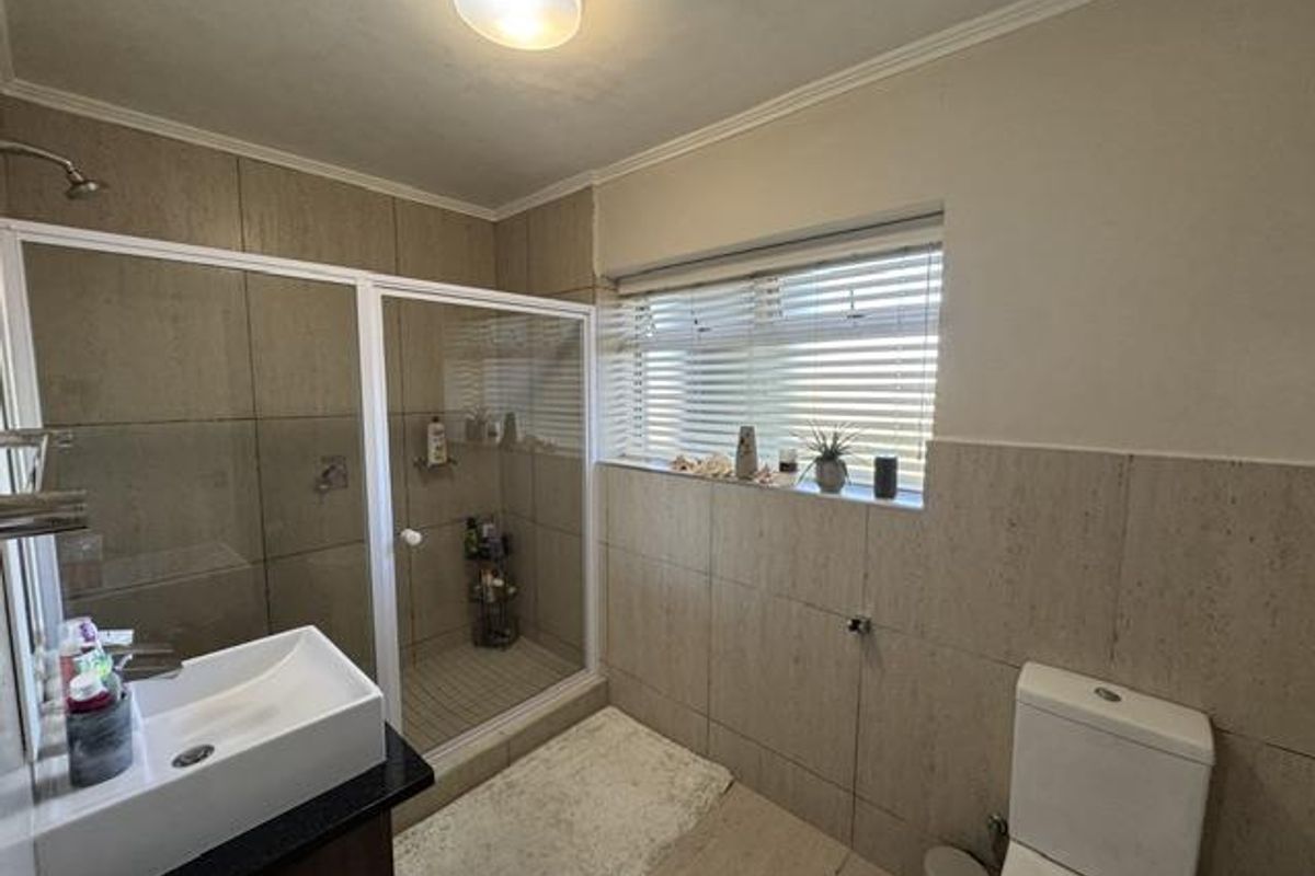 A well-maintained bathroom featuring a glass shower enclosure, modern vessel sink on a vanity, and neutral wall tiling with natural light.