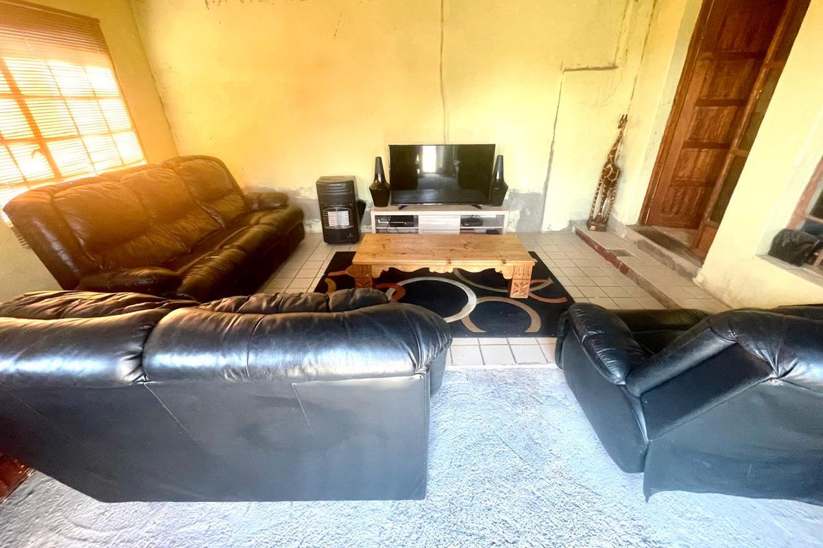 A living room space featuring tiled floors and exposed ceiling beams, currently requiring significant cosmetic renovation and wall finishing to improve the overall condition.