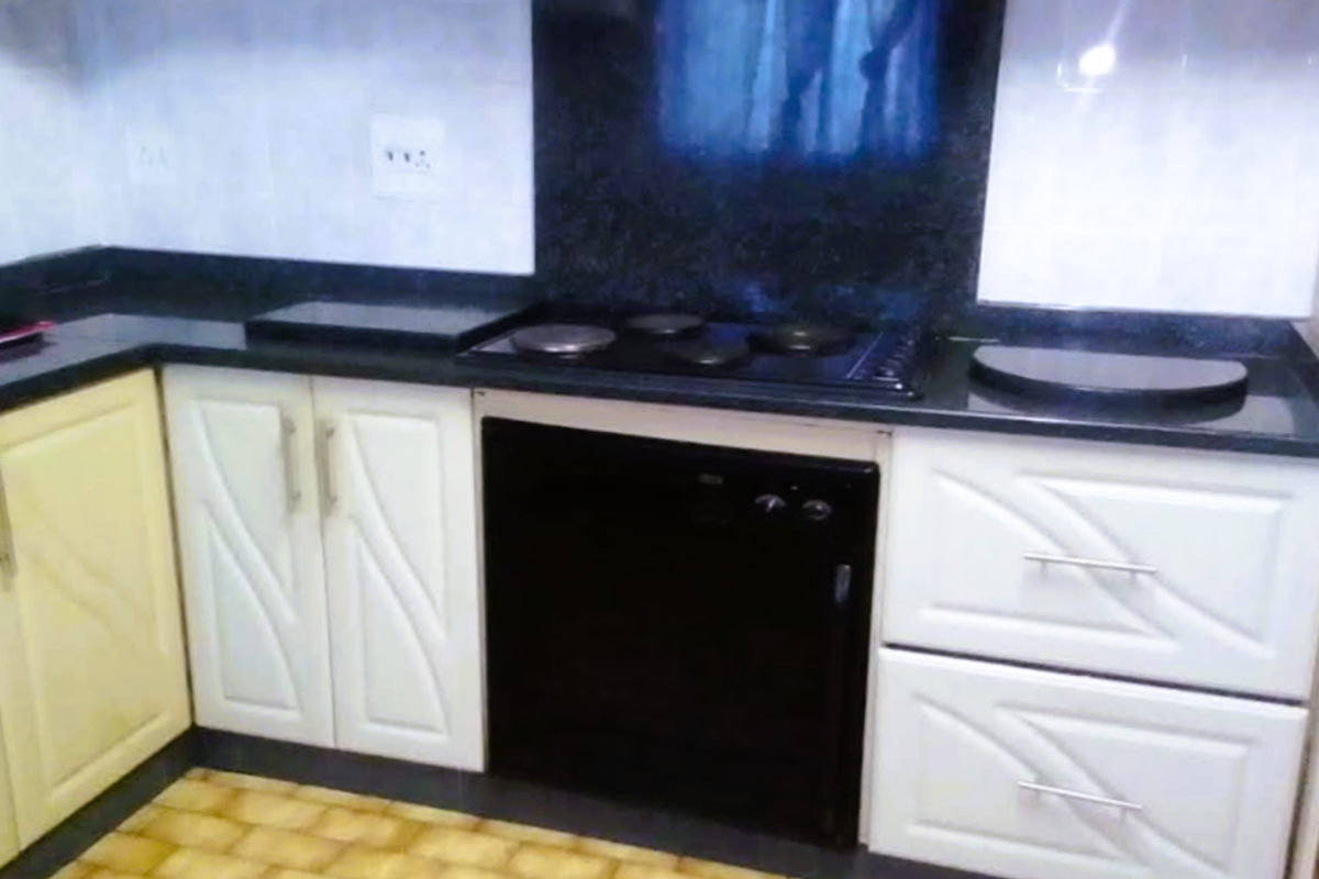 A functional kitchen area featuring built-in cabinetry, a black stone countertop, and an integrated electric hob with a matching splashback.