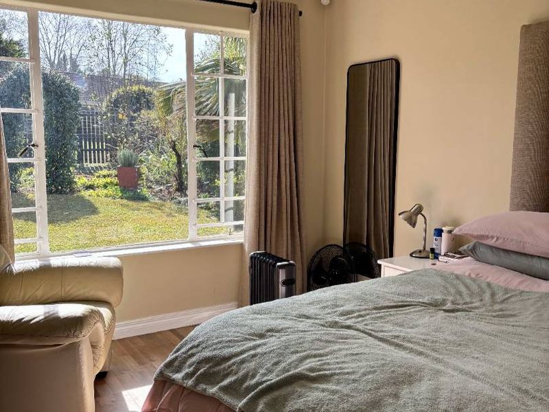 A well-lit bedroom featuring laminate flooring, a large window overlooking the garden, and classic coving detail.