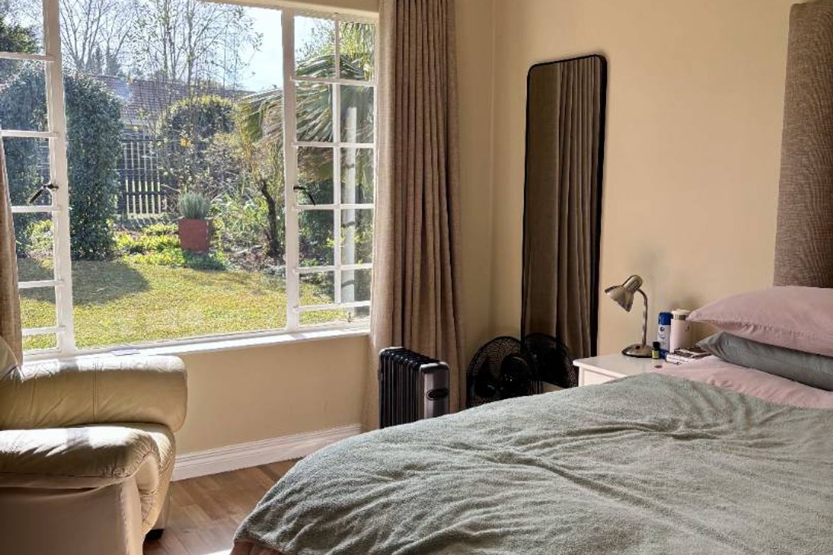 A well-lit bedroom featuring laminate flooring, a large window overlooking the garden, and classic coving detail.