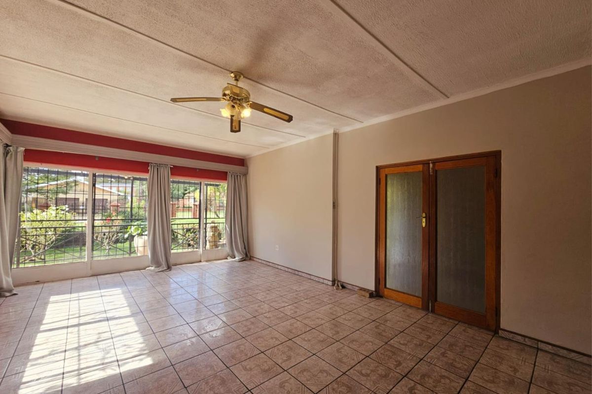 Spacious living room featuring tiled flooring, a ceiling fan, and large windows providing natural light and garden views.