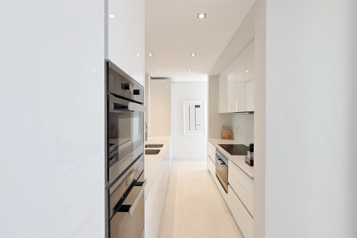 A sleek, modern galley-style kitchen featuring high-gloss white cabinetry, integrated stainless steel appliances, and recessed ceiling lighting.
