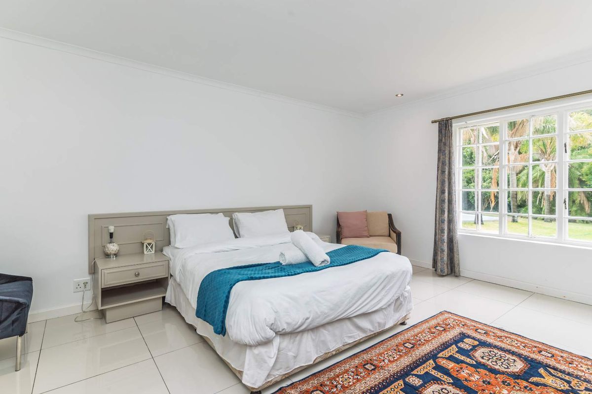 A bright and spacious bedroom featuring neutral tiled flooring, a built-in headboard, and large windows overlooking the garden.