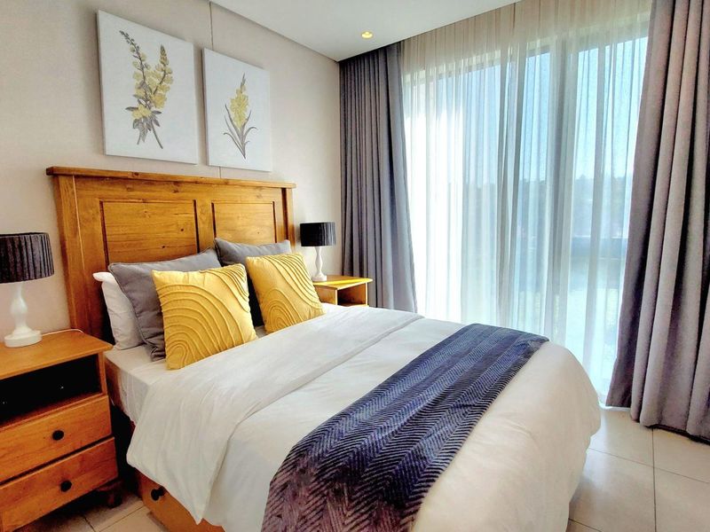 A well-maintained bedroom featuring tiled flooring, recessed lighting, and large sliding glass doors with floor-to-ceiling curtains providing ample natural light.