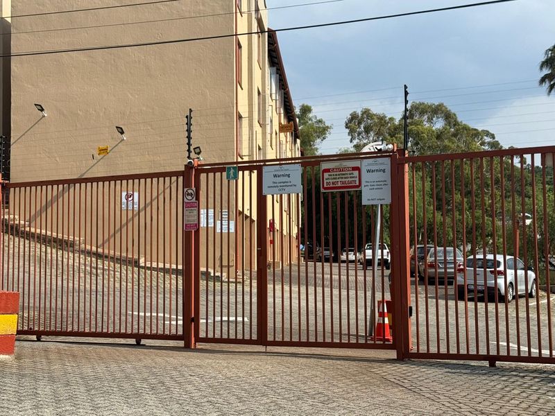 Secure gated entrance to the apartment complex featuring automated security gates, electric fencing, and CCTV surveillance.