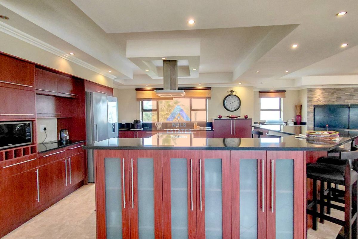 Spacious modern kitchen featuring dark wood cabinetry, granite countertops, a central island, and a stone feature wall with integrated recessed lighting.