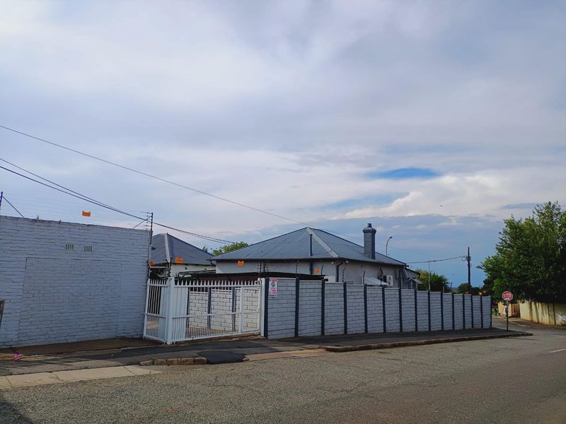 Street view of the property featuring a secure perimeter wall with electric fencing, metal gate, and a pitched metal roof.