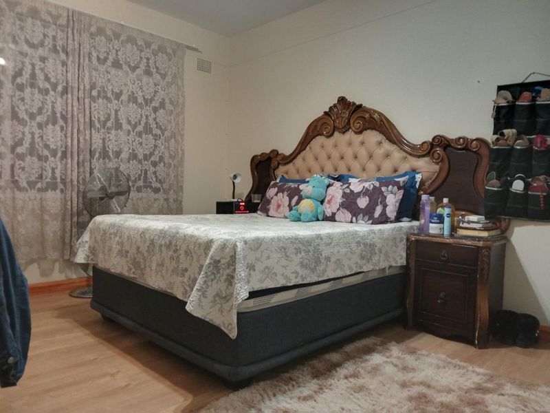 A bedroom featuring laminate flooring and a wall-mounted ventilation grille, providing a functional space for rest.