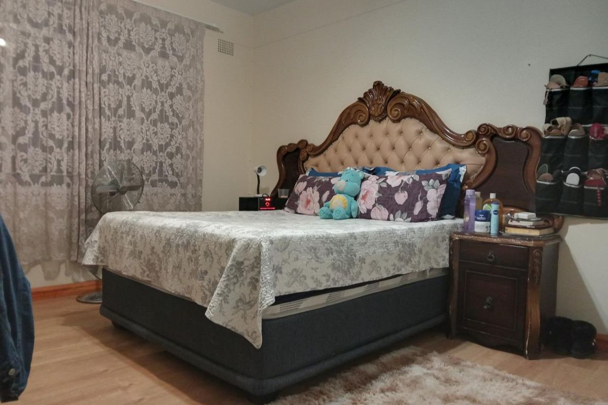 A bedroom featuring laminate flooring and a wall-mounted ventilation grille, providing a functional space for rest.