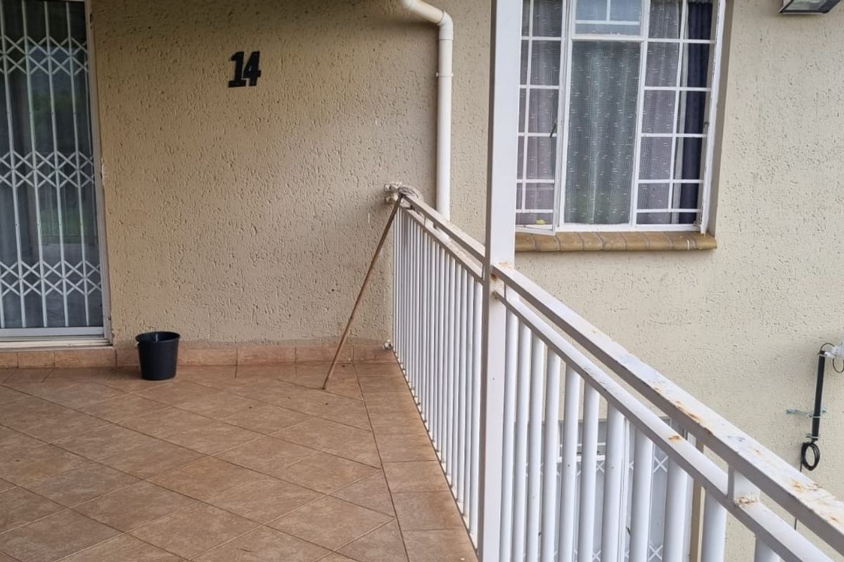 A covered balcony area featuring tiled flooring, a metal security gate, and a metal balustrade showing signs of wear and rust.