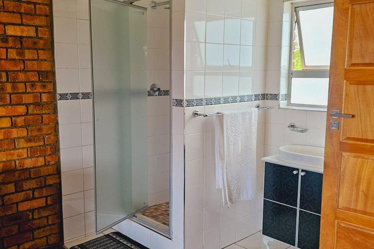 A bathroom featuring a tiled shower enclosure, a vessel sink with a vanity cabinet, and a distinctive exposed brick wall finish.