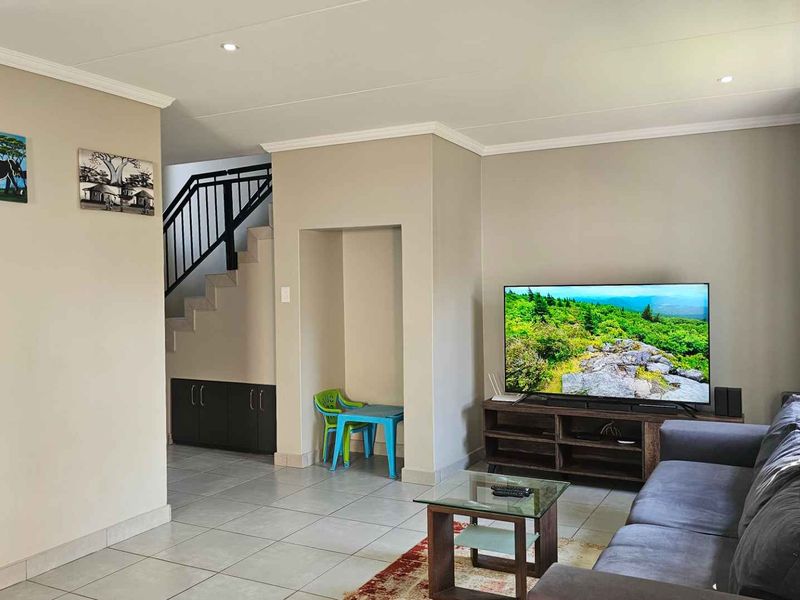 A well-maintained living room featuring tiled flooring, recessed lighting, and an integrated staircase with a metal balustrade.