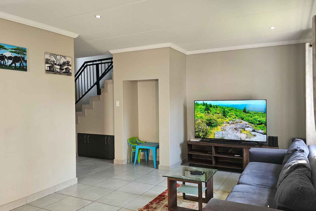 A well-maintained living room featuring tiled flooring, recessed lighting, and an integrated staircase with a metal balustrade.