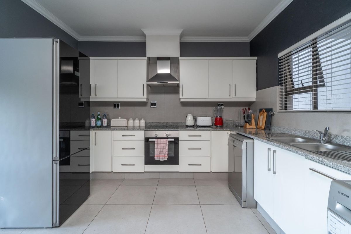 A well-maintained kitchen featuring white cabinetry, granite countertops, a built-in oven, and a stainless steel extractor fan with neutral tiled flooring.