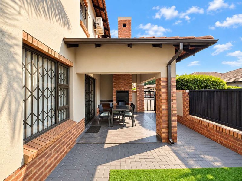A well-maintained covered patio featuring a built-in brick fireplace, tiled flooring, and brick structural pillars, providing an ideal space for outdoor entertaining.