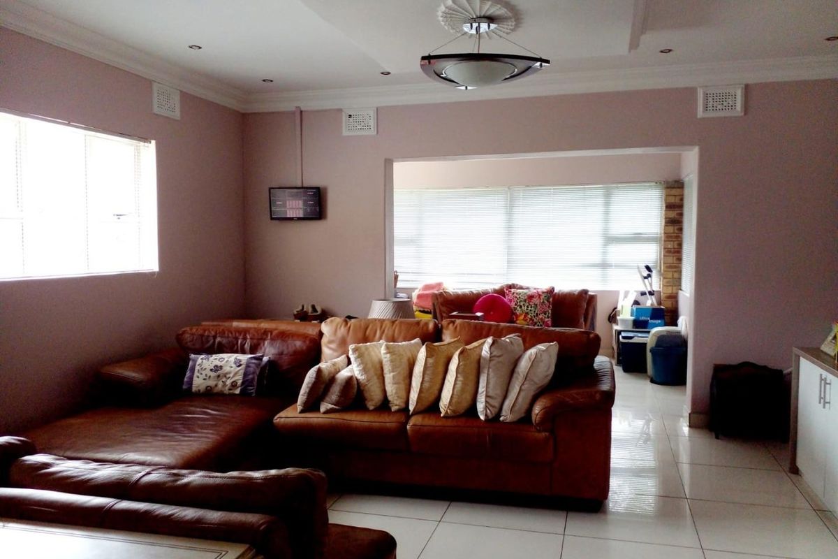 Spacious living room featuring tiled flooring, decorative ceiling rose, and recessed lighting, with an open-plan flow into an adjacent sunlit area.