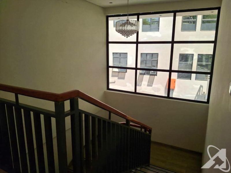 A bright stairwell featuring a modern metal balustrade with a wooden handrail and a large grid-pattern window providing ample natural light.