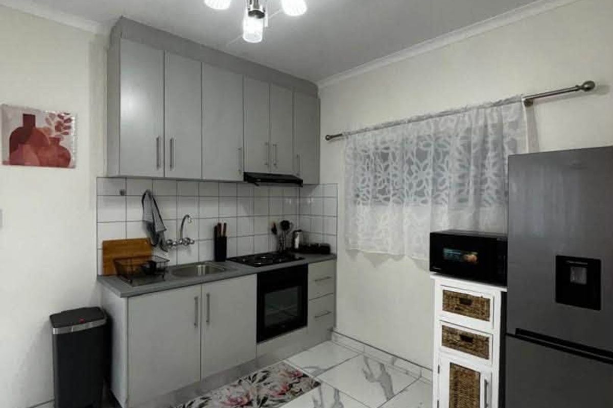 A modern kitchen featuring grey cabinetry, built-in oven, gas hob, extractor fan, and stylish marble-look floor tiles.