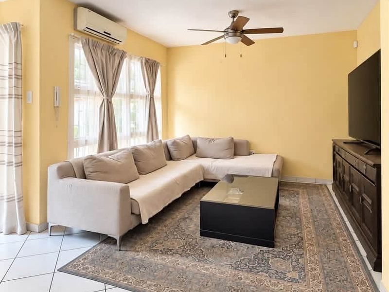 A bright living room featuring tiled flooring, a ceiling fan, and a wall-mounted split-system air conditioner.