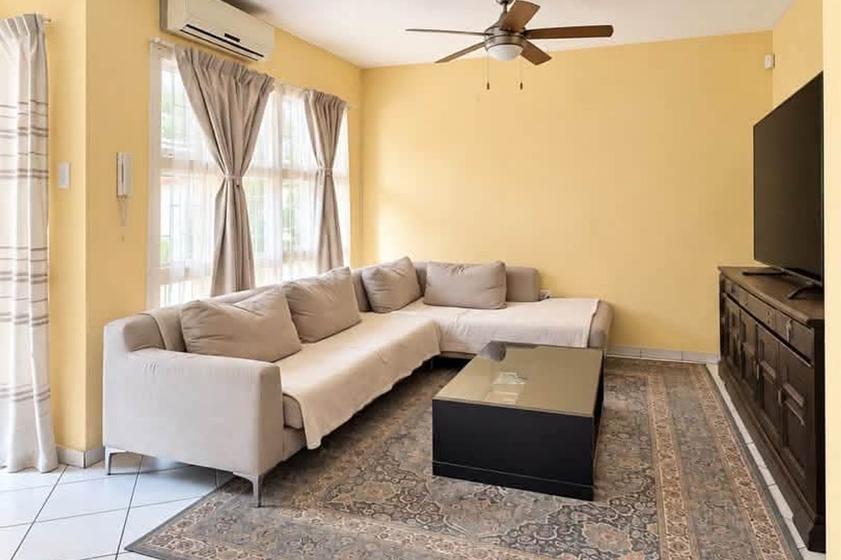 A bright living room featuring tiled flooring, a ceiling fan, and a wall-mounted split-system air conditioner.
