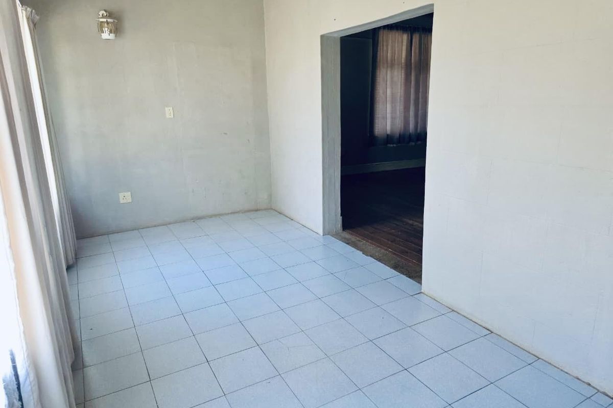 An empty living room featuring tiled flooring and a doorway leading to an adjacent room with wooden floors.